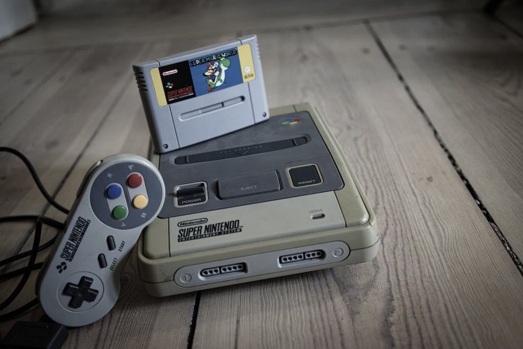 From above of aged video game console with cassette and controller with colorful buttons on wooden surface